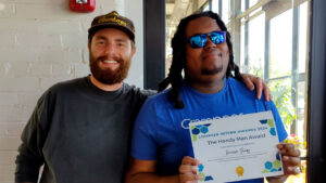2 men smiling at camera with award in front of them.